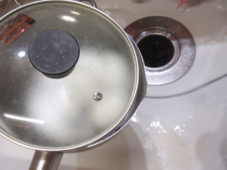 固ゆで卵の殻の剥き方　鍋の蓋をずらして押え、お湯を捨てます。