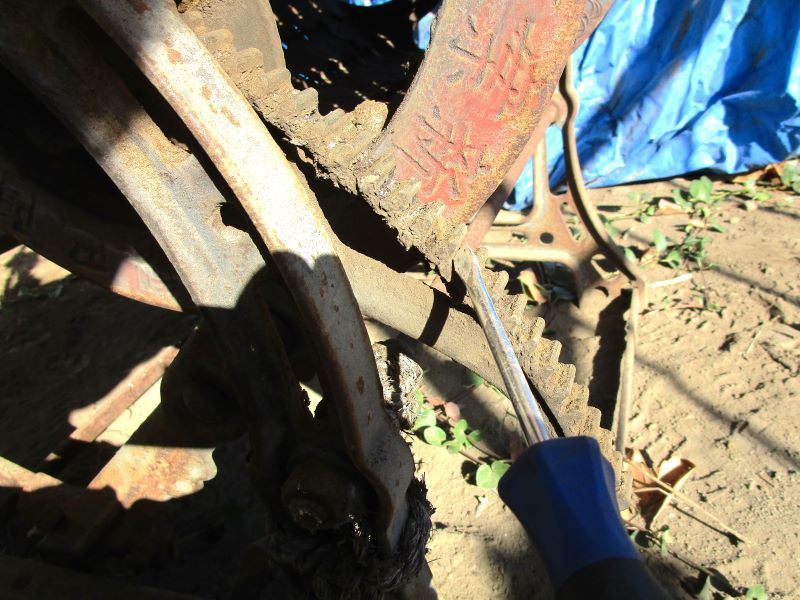 京都西陣巴製作所製・足踏み式脱穀機　の修理・再生作業①こびりついていた土汚れのかたまりをマイナスドライバーでこそぎ落とします。