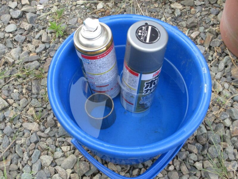 バケツのお湯でスプレー缶を湯煎する際、倒れないよう固定する工夫