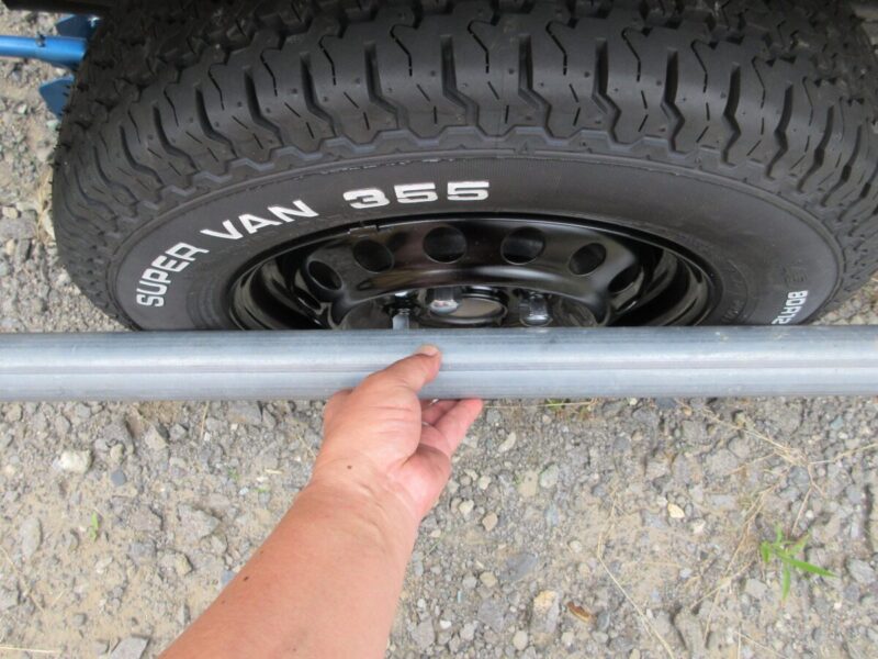 ハイゼットトラックの純正ホイール・ホワイトレタータイヤに単管パイプを縦に当て、全長22mmのショートメッキナットがタイヤのサイドウォールよりも内側に収まっていることを確認している様子。