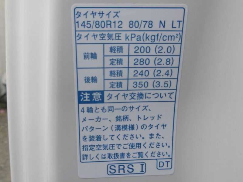 ダイハツ・ハイゼットトラックの運転席ドア開口部に貼り付けられた、タイヤサイズ「145/80R12 80/78N LT」と、積載量に応じた推奨空気圧（前輪200-280kPa、後輪240-350kPa）が記載されたコーションプレートの写真。