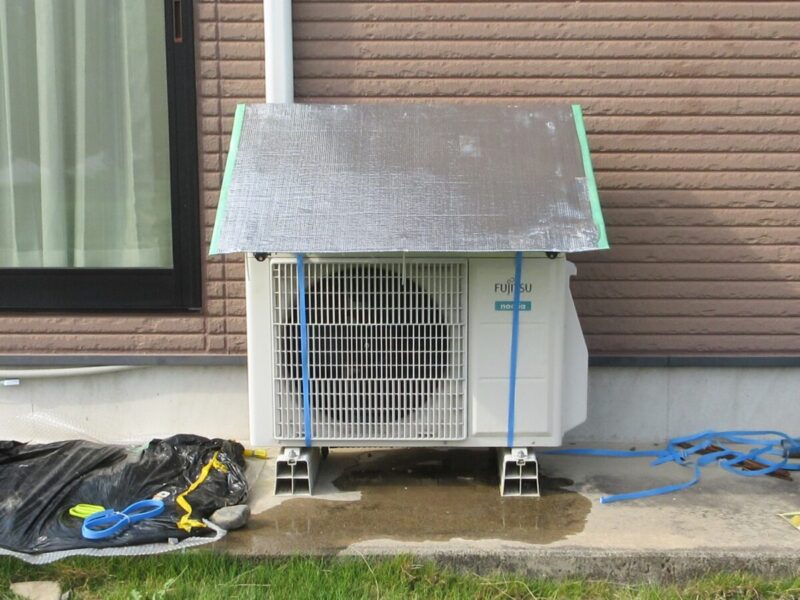 自作の日よけカバーを室外機の上に戻し、ドレンホースや排水気化装置の大部分が日よけの陰に隠れてすっきりと設置されたエアコン室外機の全体写真。